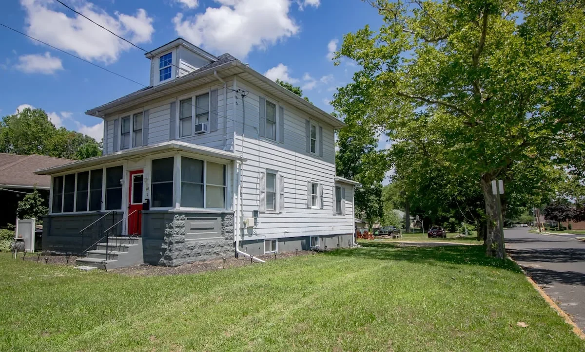 The Zen Den from the side yard: a two-story home with a screened porch, a red door and a big lawn
